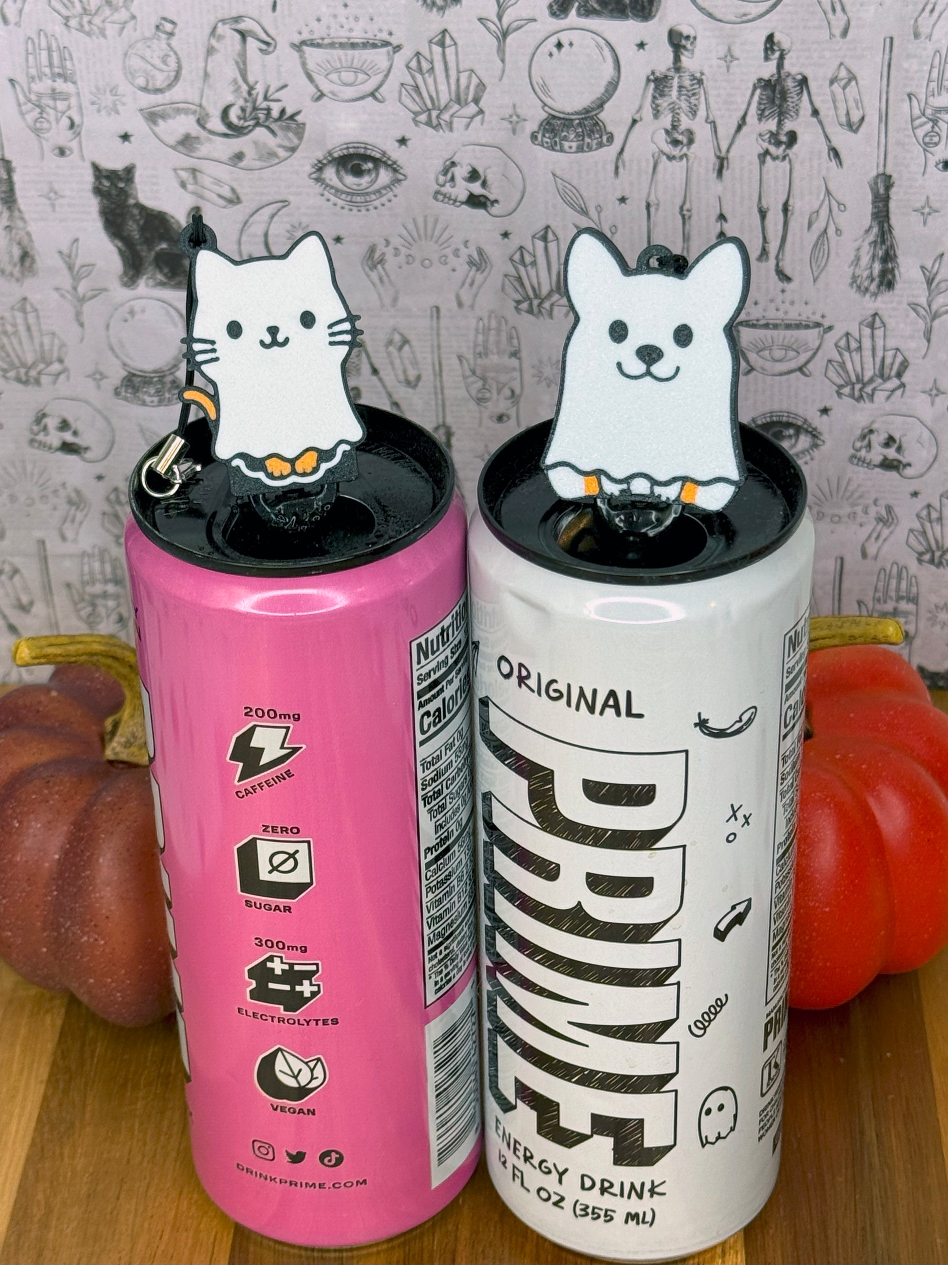 Two energy drink cans with ghost caat and ghost dog Tab Buddies on a wooden surface.