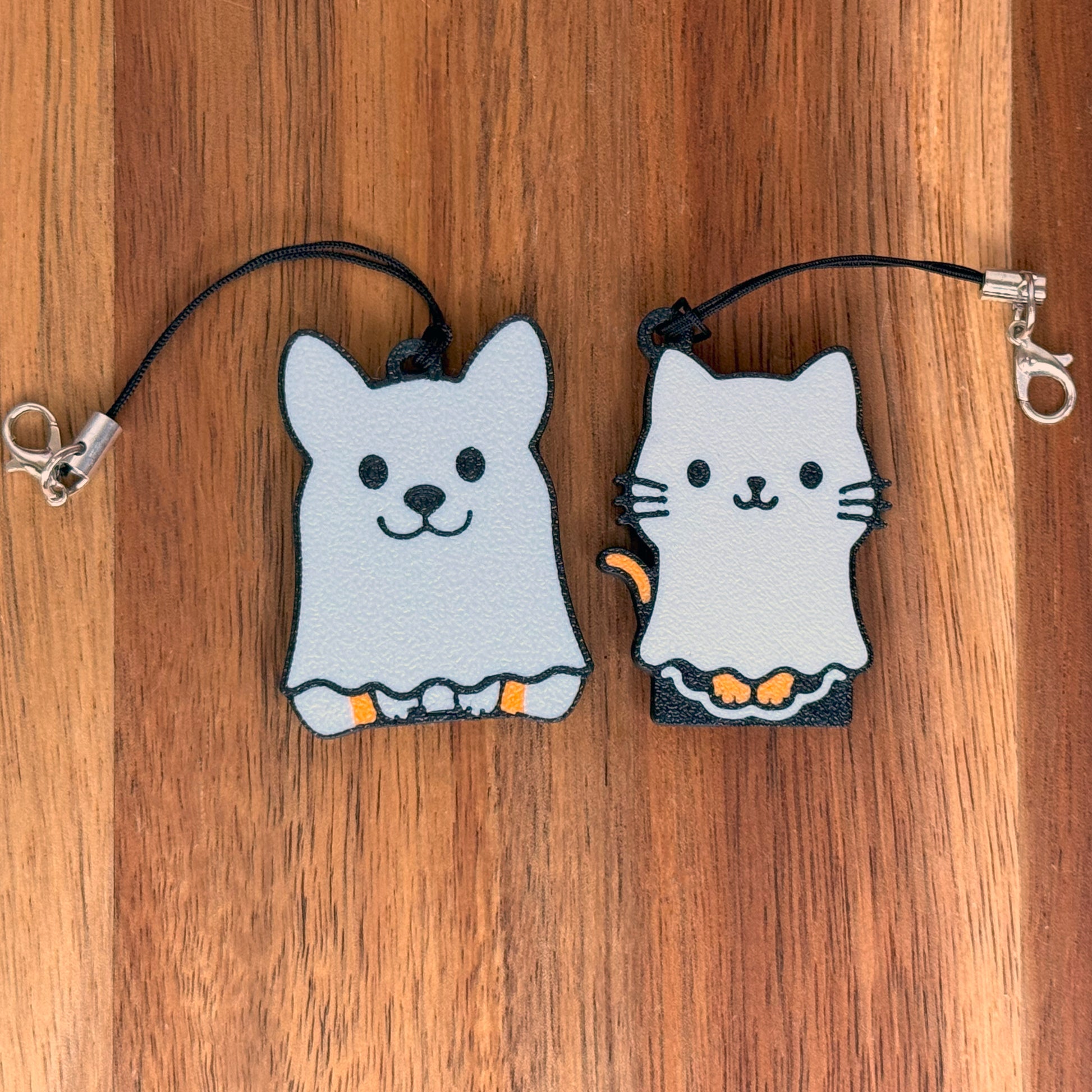 Two ghost-shaped cat and dog Tab Buddy keychains on a wooden surface