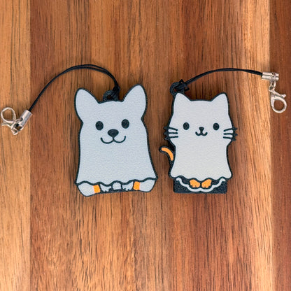 Two ghost-shaped cat and dog Tab Buddy keychains on a wooden surface