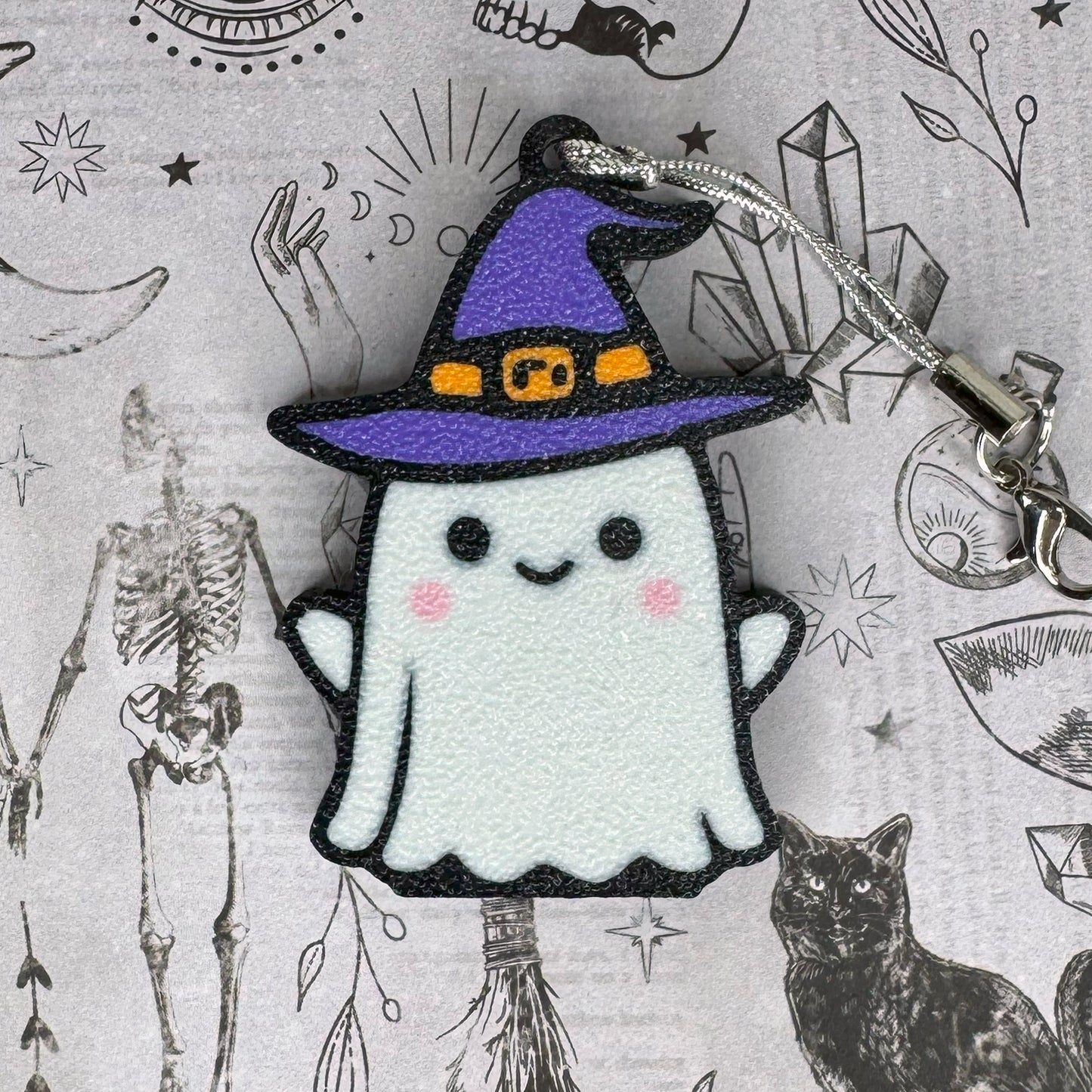 Ghost Tab Buddy keychain with a purple witch hat on a Halloween-themed background