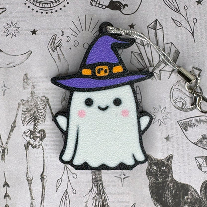 Ghost Tab Buddy keychain with a purple witch hat on a Halloween-themed background