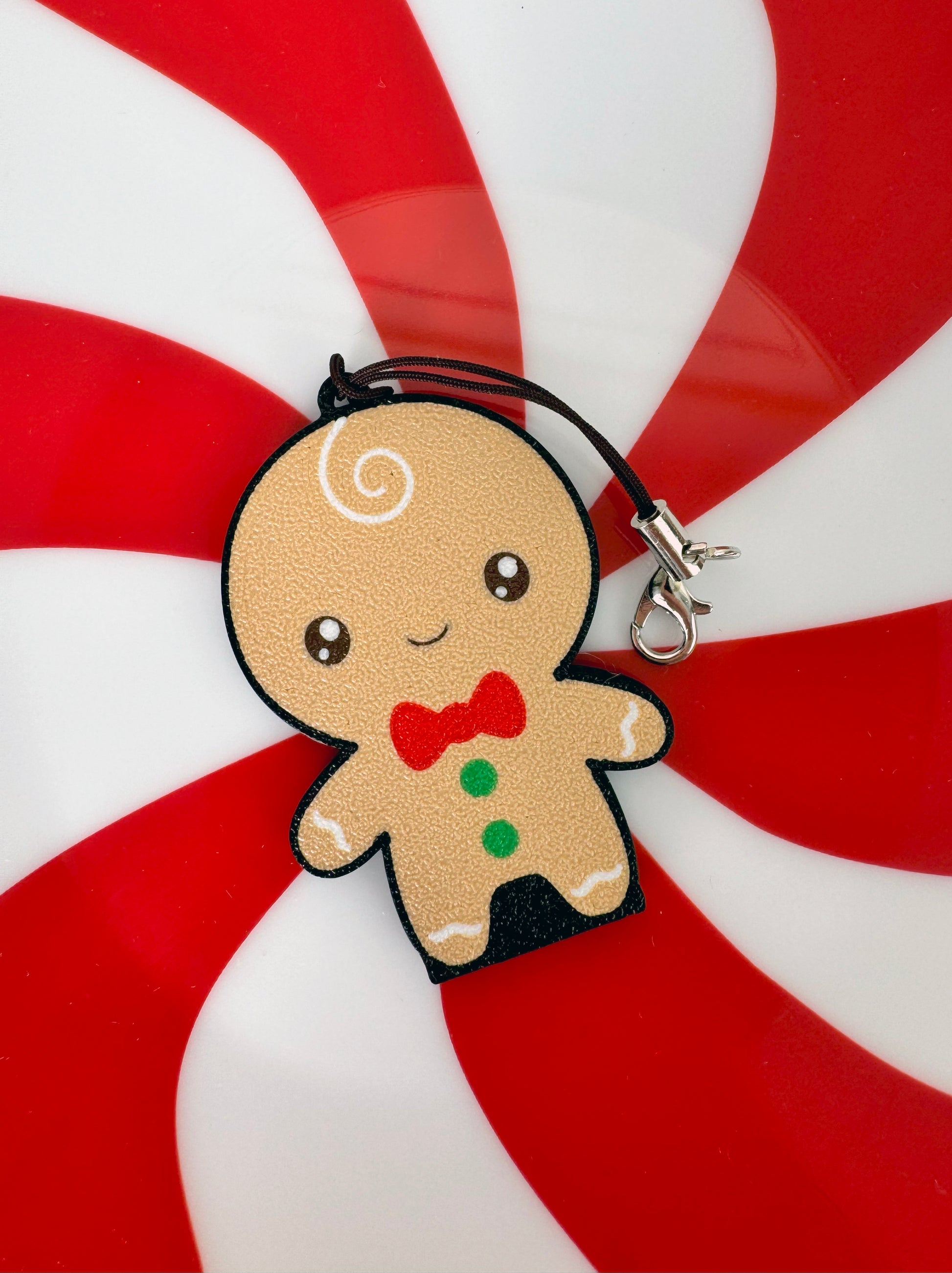 Gingerbread man Tab Buddy keychain with a bow tie on a peppermint candy background