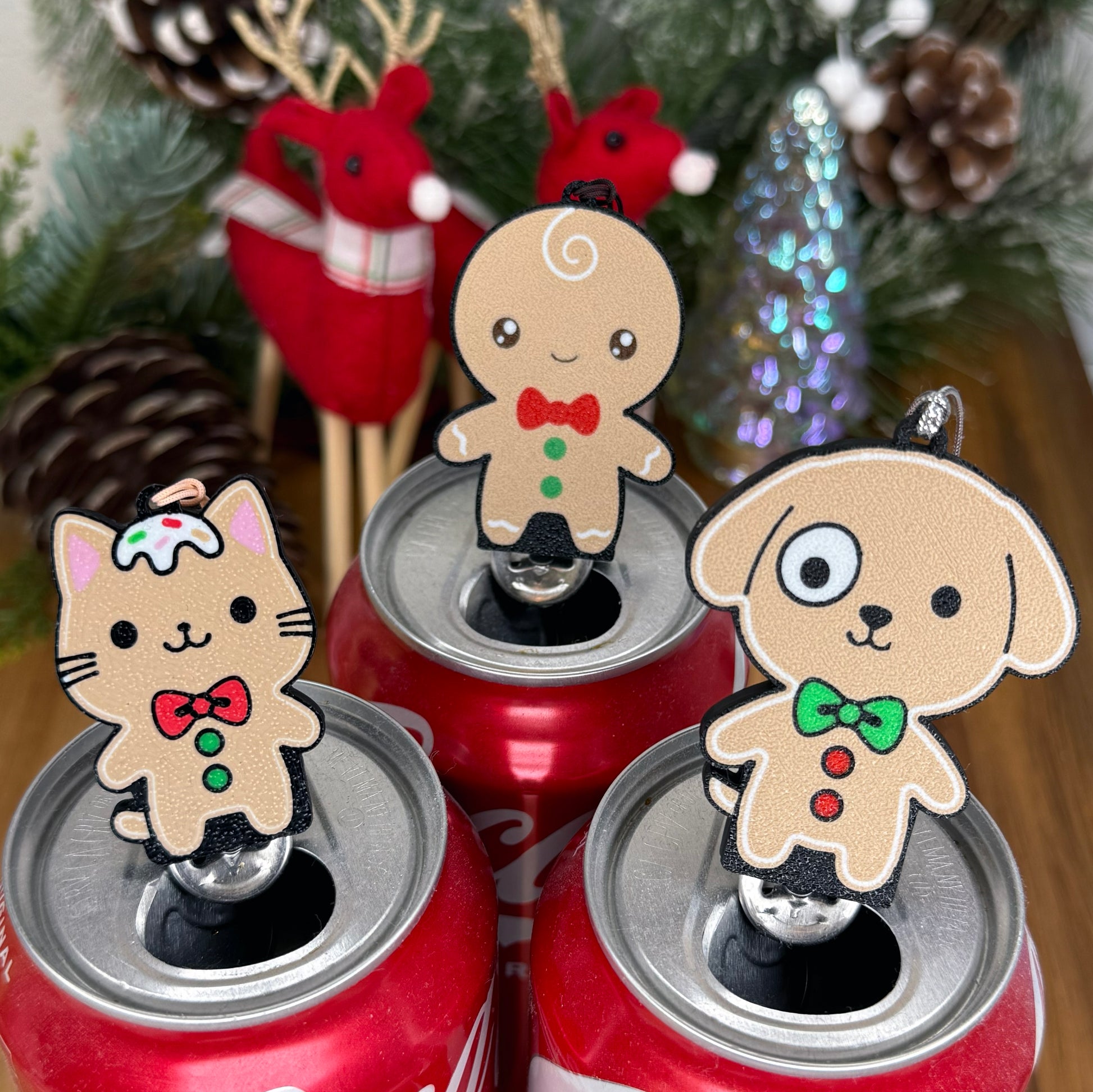Three cans with gingerbread themed Tab Buddies against a Christmas tree background