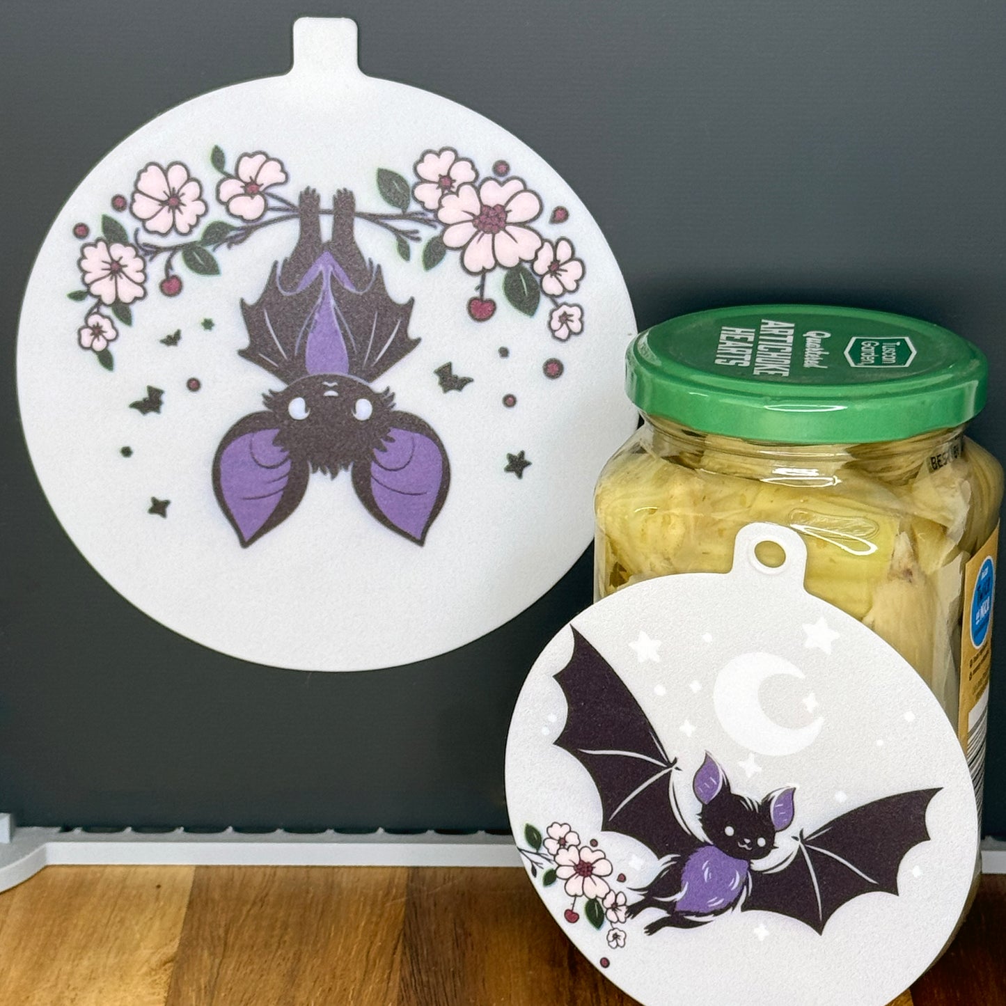 Two silicone Grippy Pads with bat designs on a jar and a black surface.