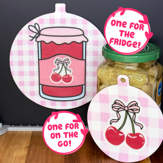 Two silicone Grippy Pads with cherry jam-themed gingham designs on a jar and a black surface, with text 'One for the Fridge!' and 'One for On the Go!'.