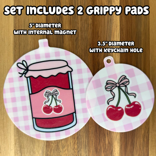 Two cherry jam design-themed circular grippy pads on a wooden background with text indicating set details -- The set includes 2 Grippy Pads: one 5" diameter with an internal magnet and one 3.5" diameter with a keychaini hole.