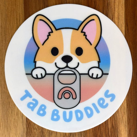 Circular grippy  pad with a cartoon corgi holding a tab and 'Tab Buddies' text on a wooden surface