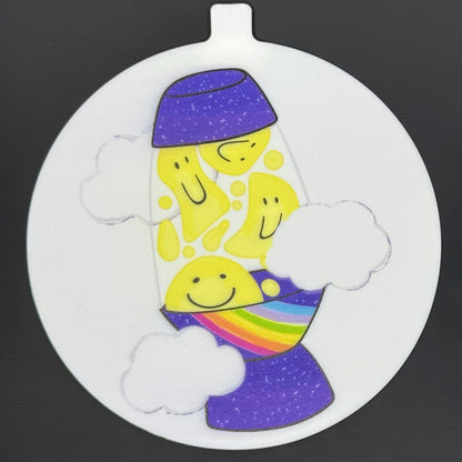 The large 5" diameter size Grippy Pad of the Groovy Pride set is shown against a grey background. The design  includes an internal magnet in a tab at the top and features a purple galaxy lava lamp with yellow smiley faces in the lava, a rainbow along one edge and clouds surrounding it.