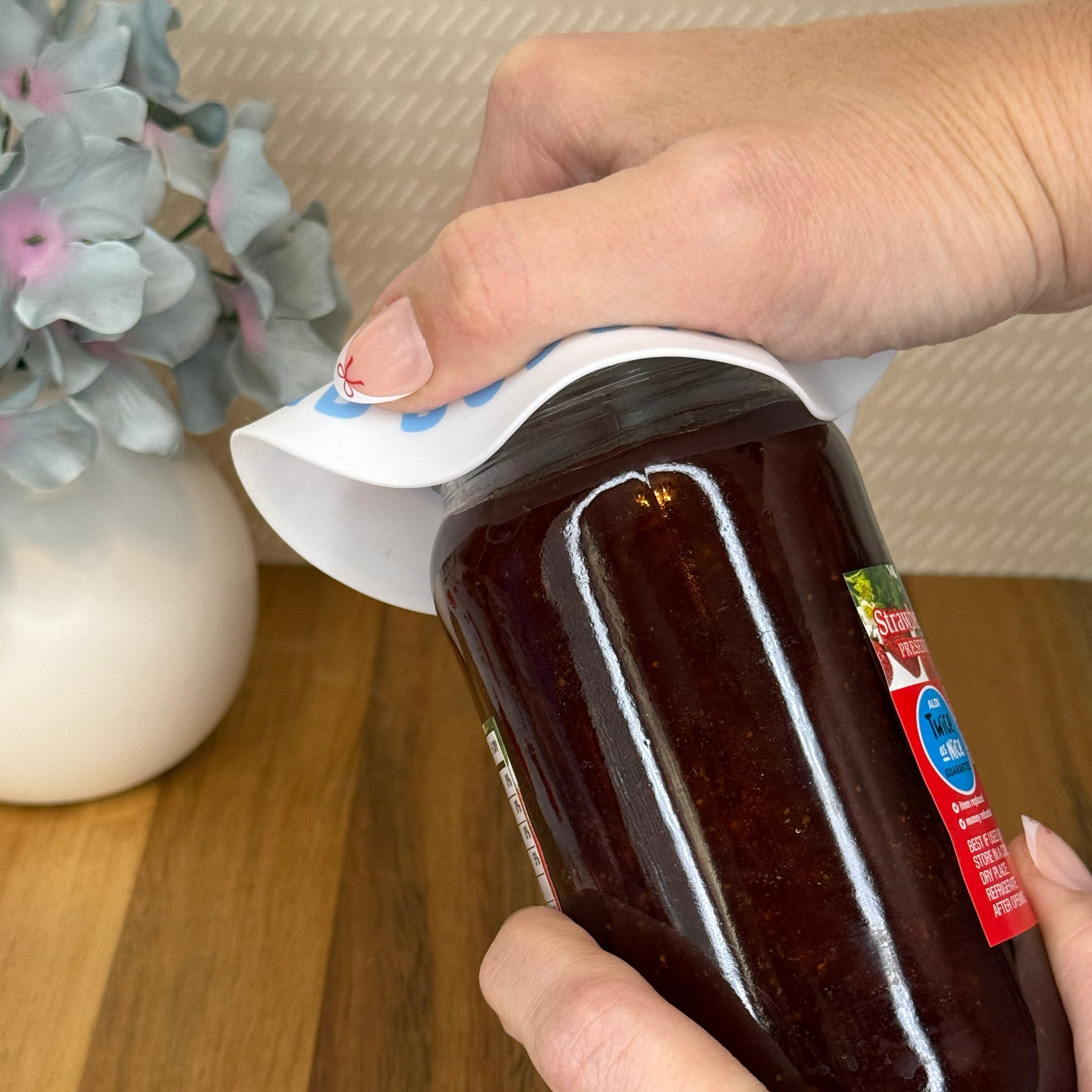 Person using a Tab Buddies grippy pad to help open a jar of strawberry preserves.