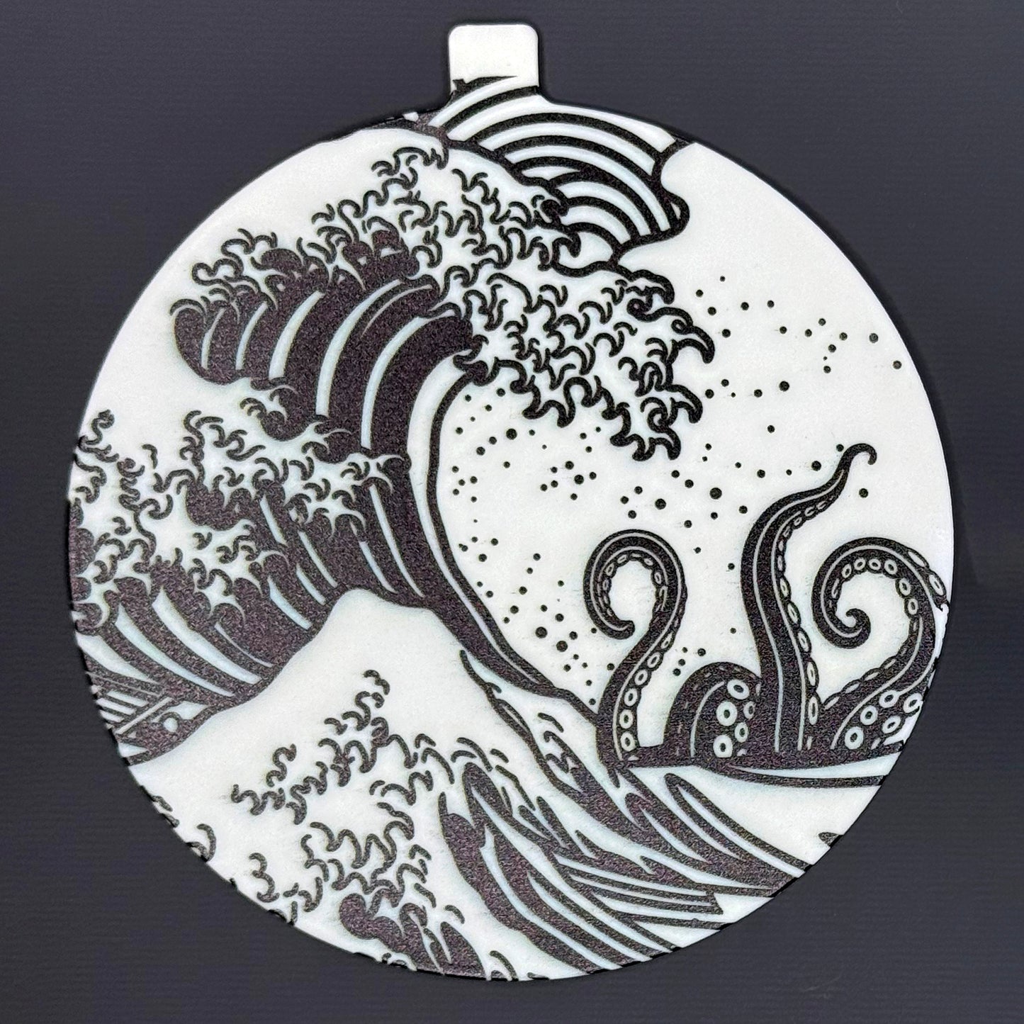 The large 5" diameter size Grippy Pad of the Kraken Wave set is shown against a grey background. The design  includes an internal magnet in a tab at the top and features the famous Great Wave off Kanagawa desigin in black-and-white with kraken tentacles rising above the wave.
