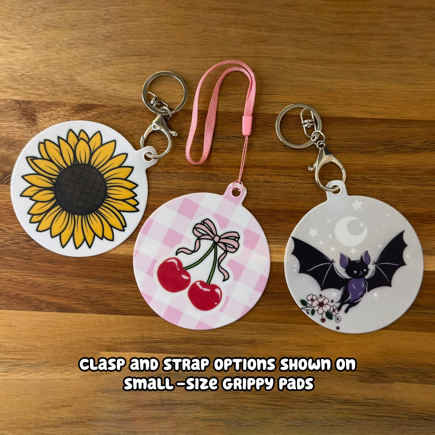 Three round Grippy Pads with different designs on a wooden surface, showing clasp and strap options.
