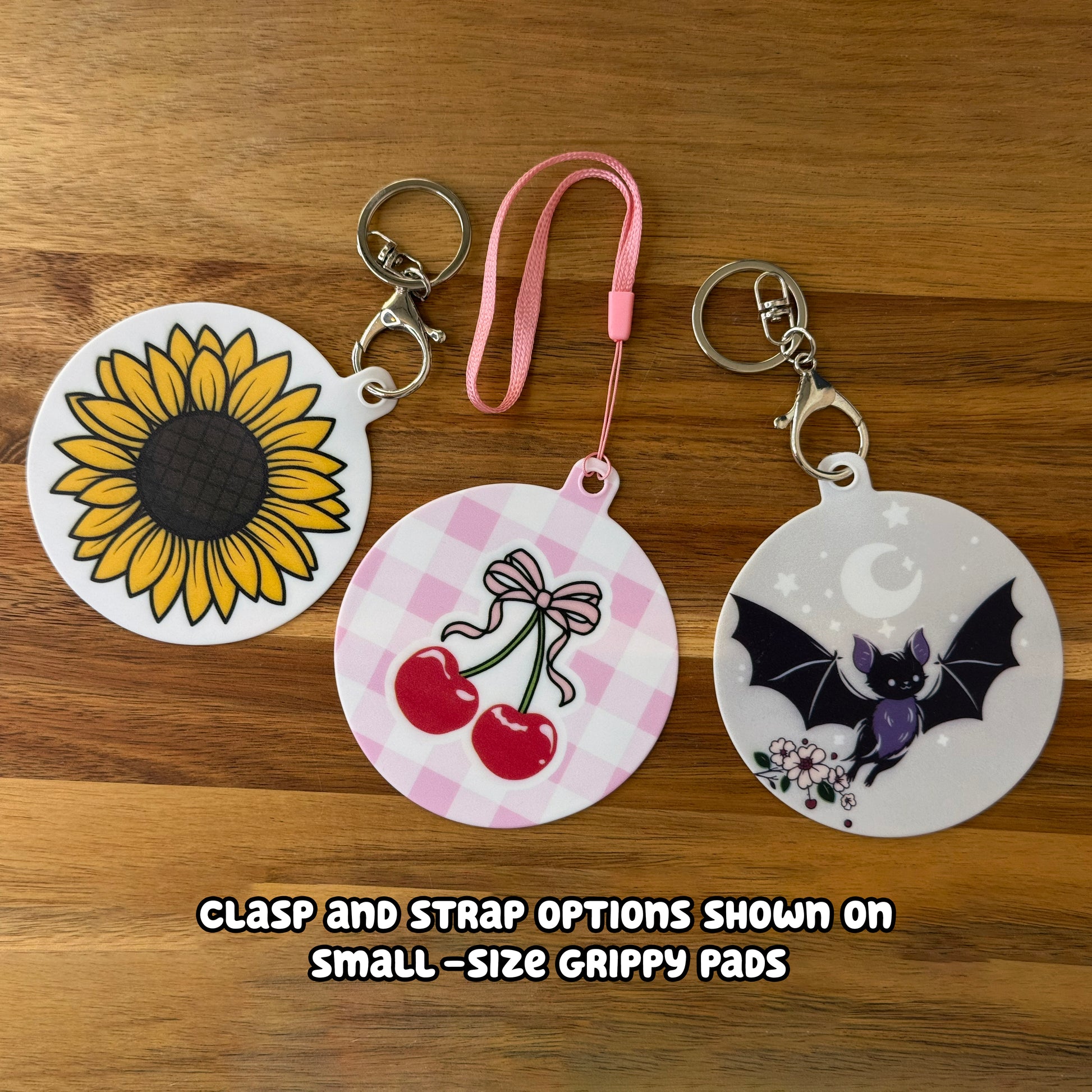 Three round Grippy Pads with different designs on a wooden surface, showing clasp and strap options.