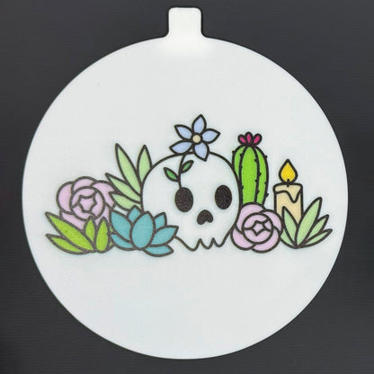 The large 5" diameter size Grippy Pad of the Mystic Garden set is shown against a grey background. The design  includes an internal magnet in a tab at the top and features a garden of cacti, succulents, a candle and flowers with a skull.