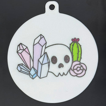 The small 3.5" diameter size Grippy Pad of the Mystic Garden set is shown against a grey background. The design  includes a keychain hole set into a tab at the top and features a skull, cactus, flower and colorful crystals.