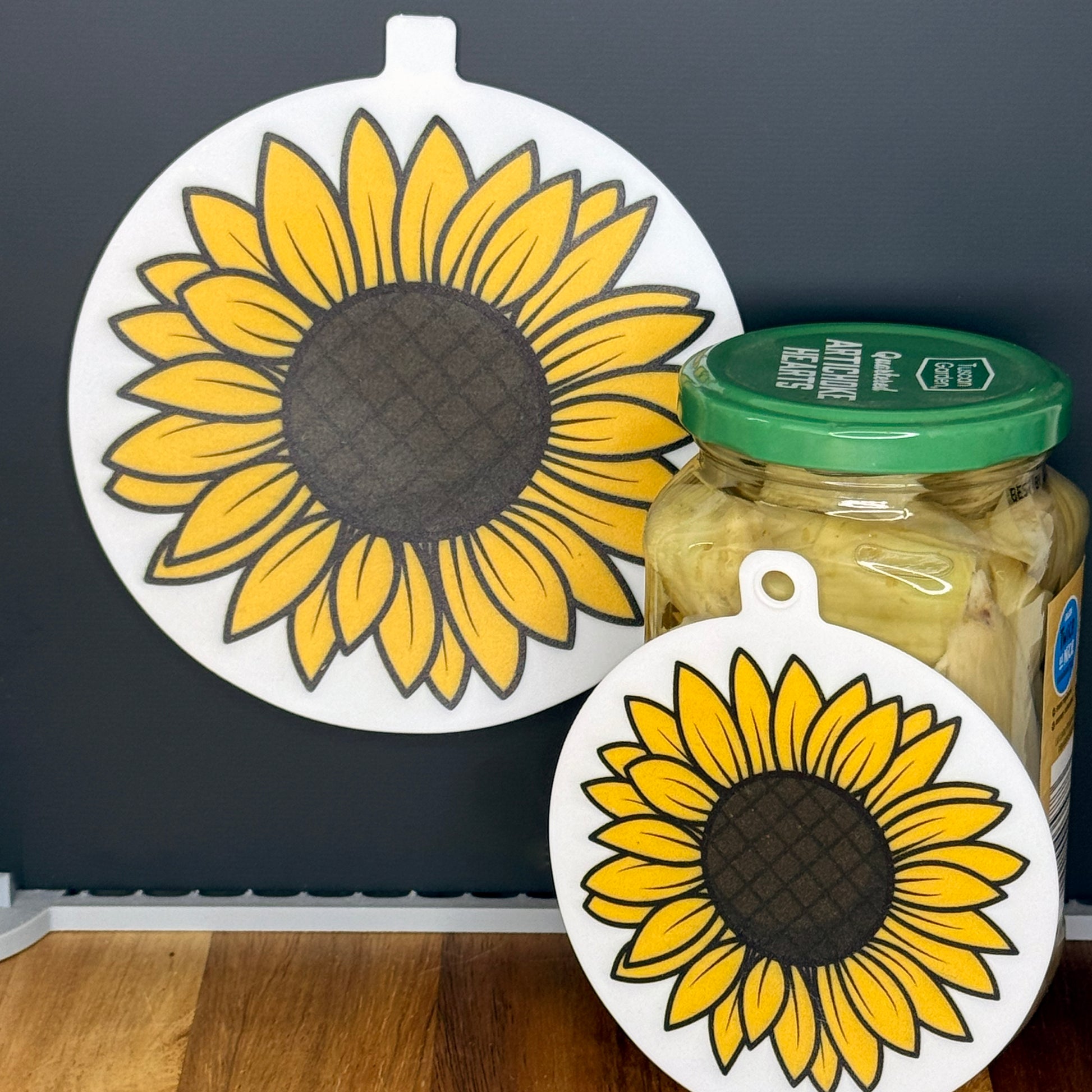 Two silicone Grippy Pads with sunflower designs on a jar and a black surface.