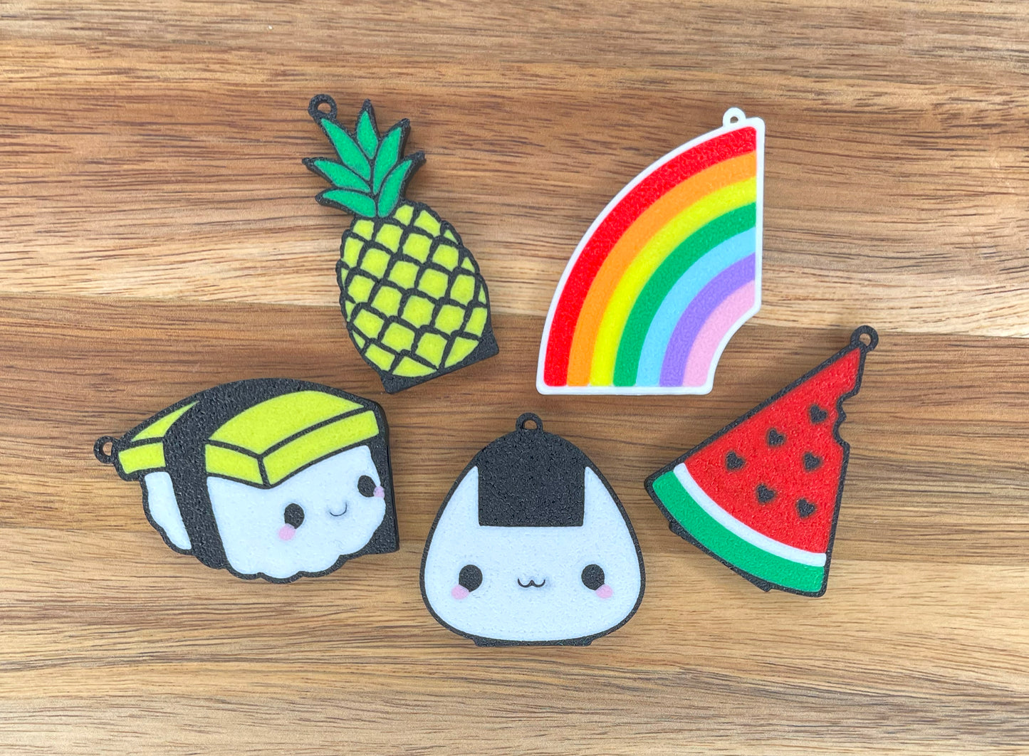 Set of colorful Tab Buddies including a pineapple, rainbow, watermelon, and sushi on a wooden surface.