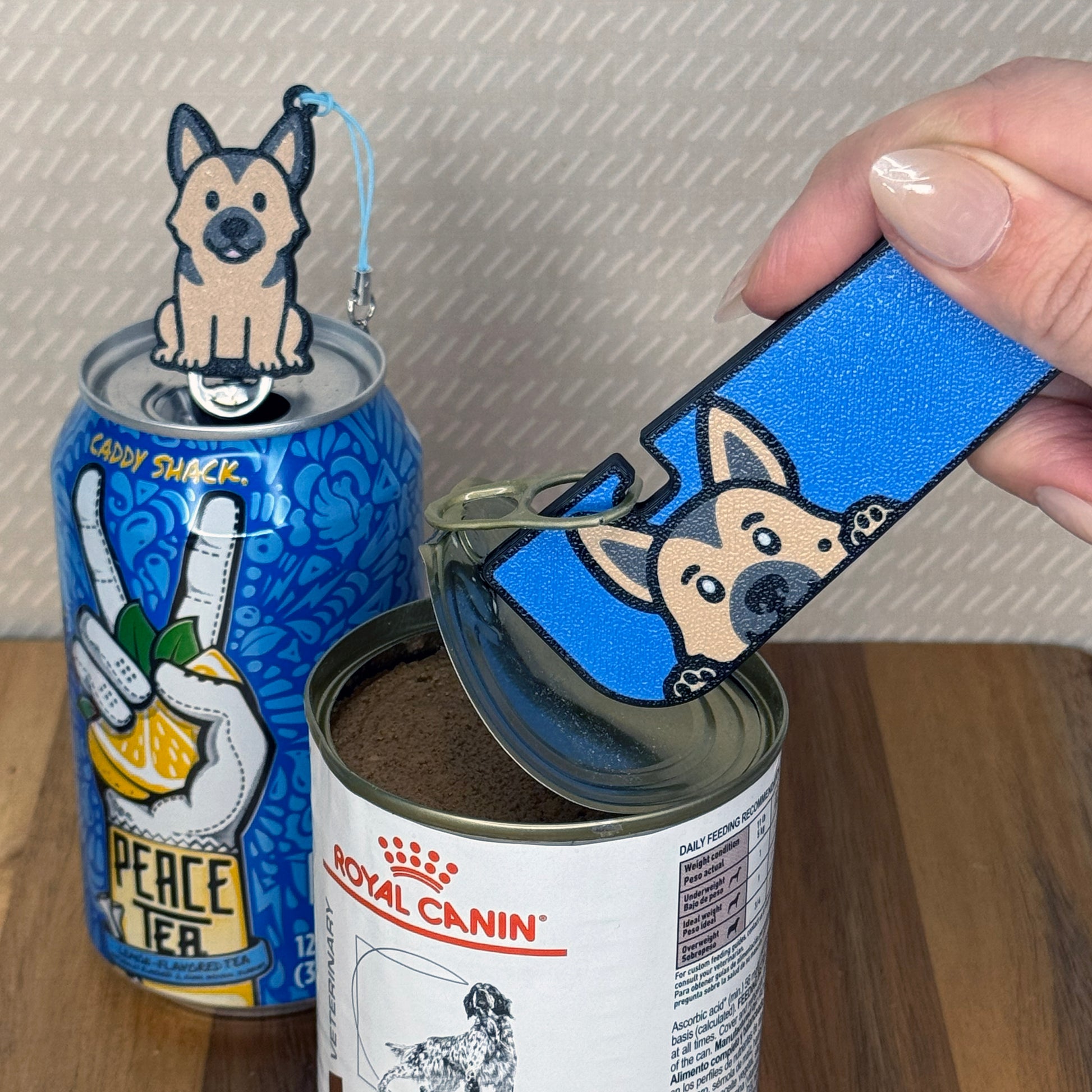 A matching set of German Shepherd-inspired Tab Buddies are shown. The soda-sized Tab Buddy rests atop a blue soda can, and the Tab Buddy XL is used to peel back a can of dog food.