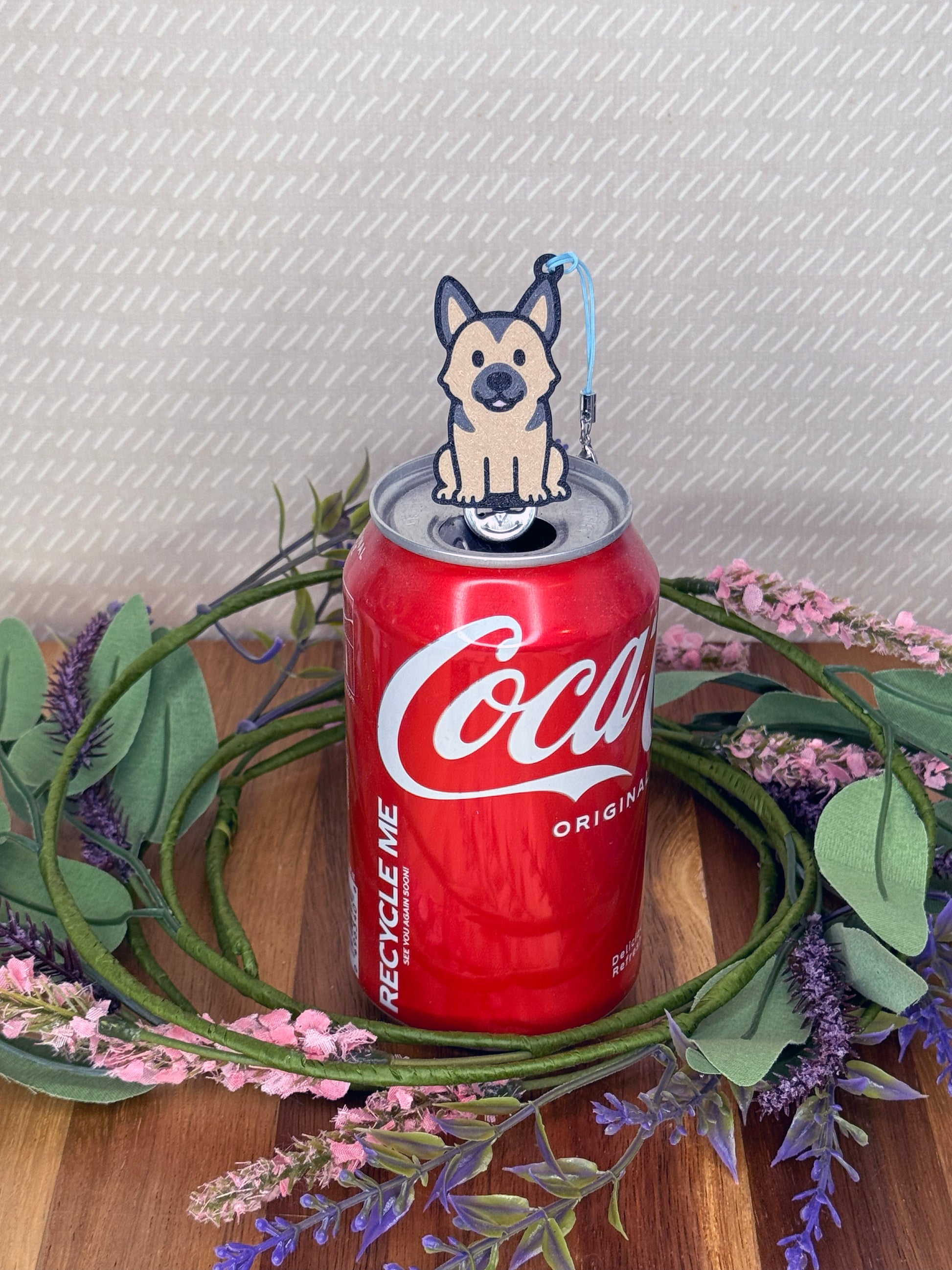 A tan and brownd German Shepherd-inspired Tab Buddy rests atop an open can tab with a beige background and floral accents.