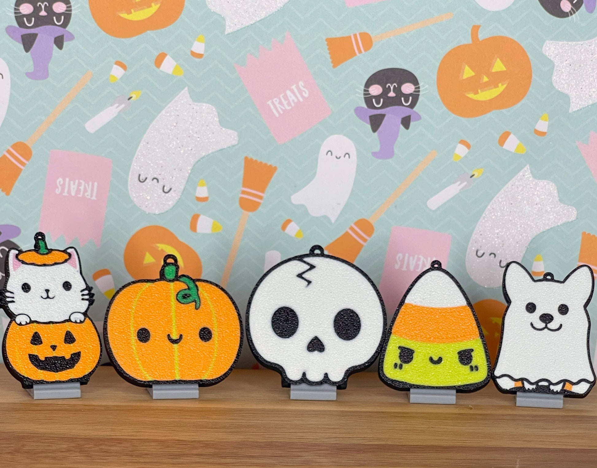 Set of Halloween-themed Tab Buddies including pumpkins, ghosts, and a skull on a wooden surface with a light blue background featuring Halloween decorations.