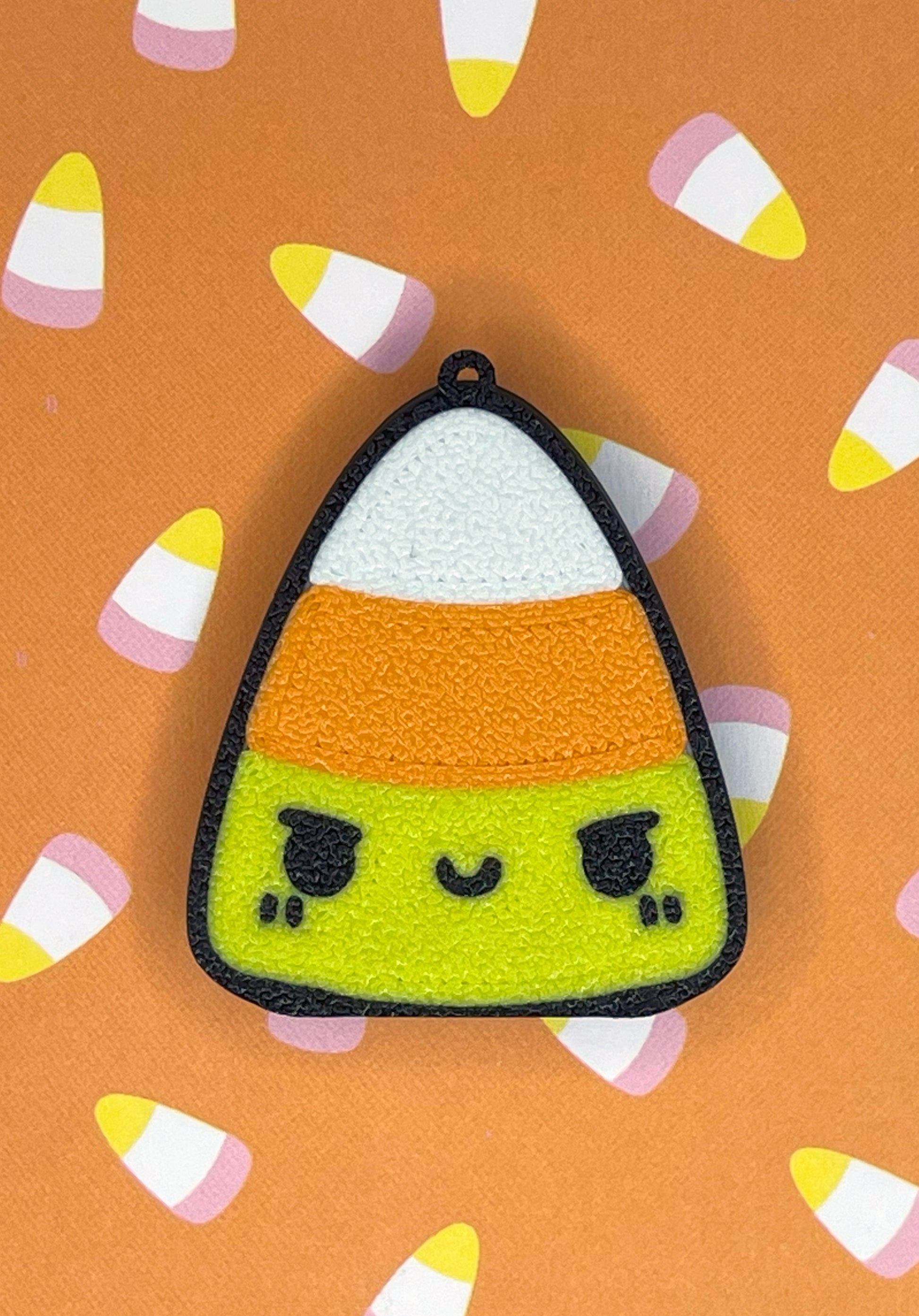 Candy corn-shaped Tab Buddy with a face on an orange background with candy corn patterns