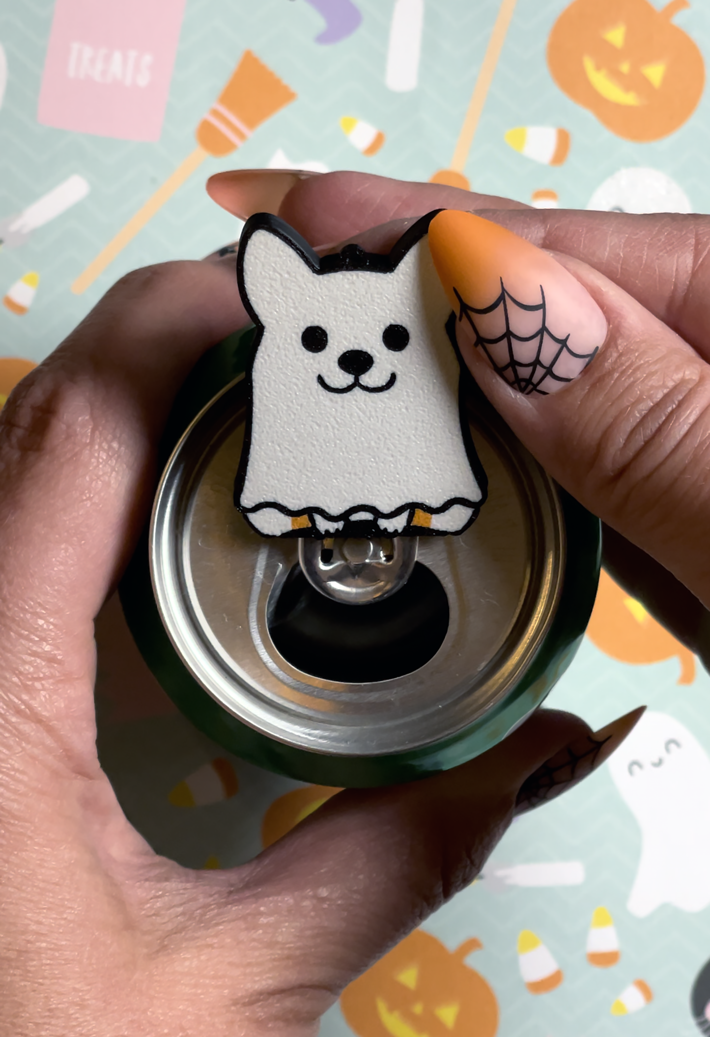 Hand with long nails holding a ghost dog Tab Buddy  against a Halloween-themed background