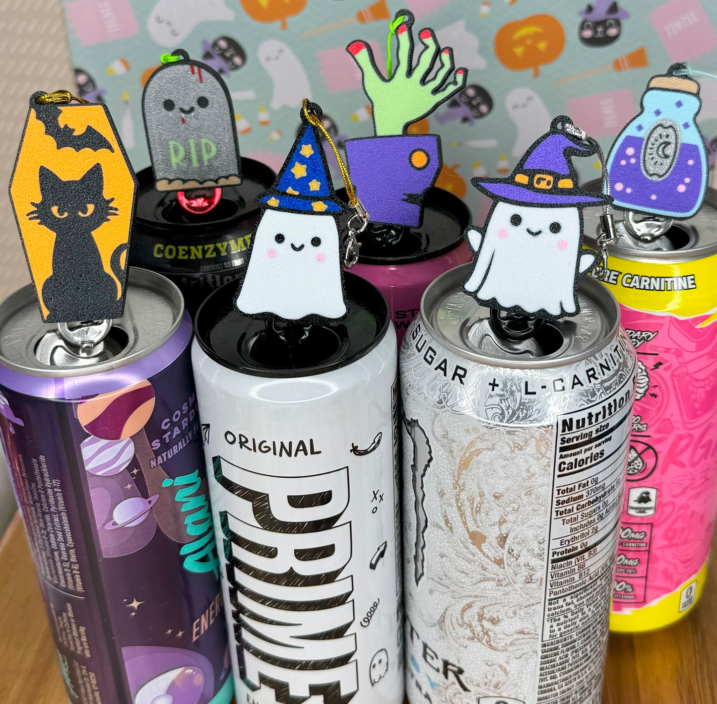 Halloween-themed Tab Buddy keychains rest on top of energy drink cans with Halloween-themed designs.