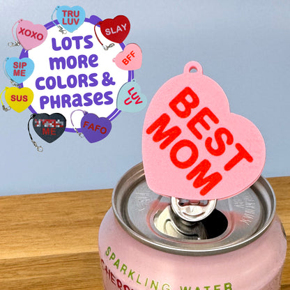 Pink can with 'BEST MOM' heart-shaped Tab Buddy on a light blue background. Text reads "Lots more colors and phrases."