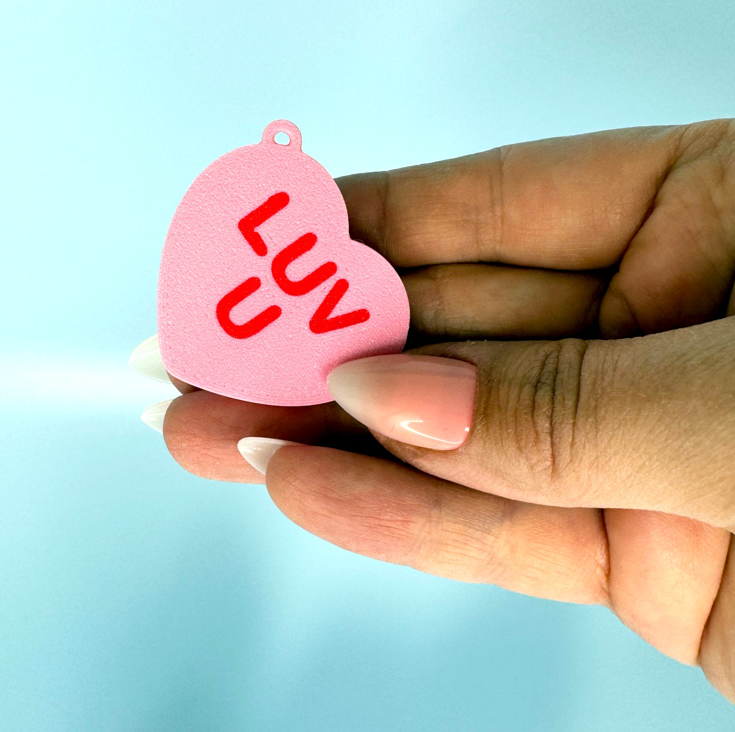 Heart-shaped pink Tab Buddy with 'LUV U' text held in a hand against a light blue background