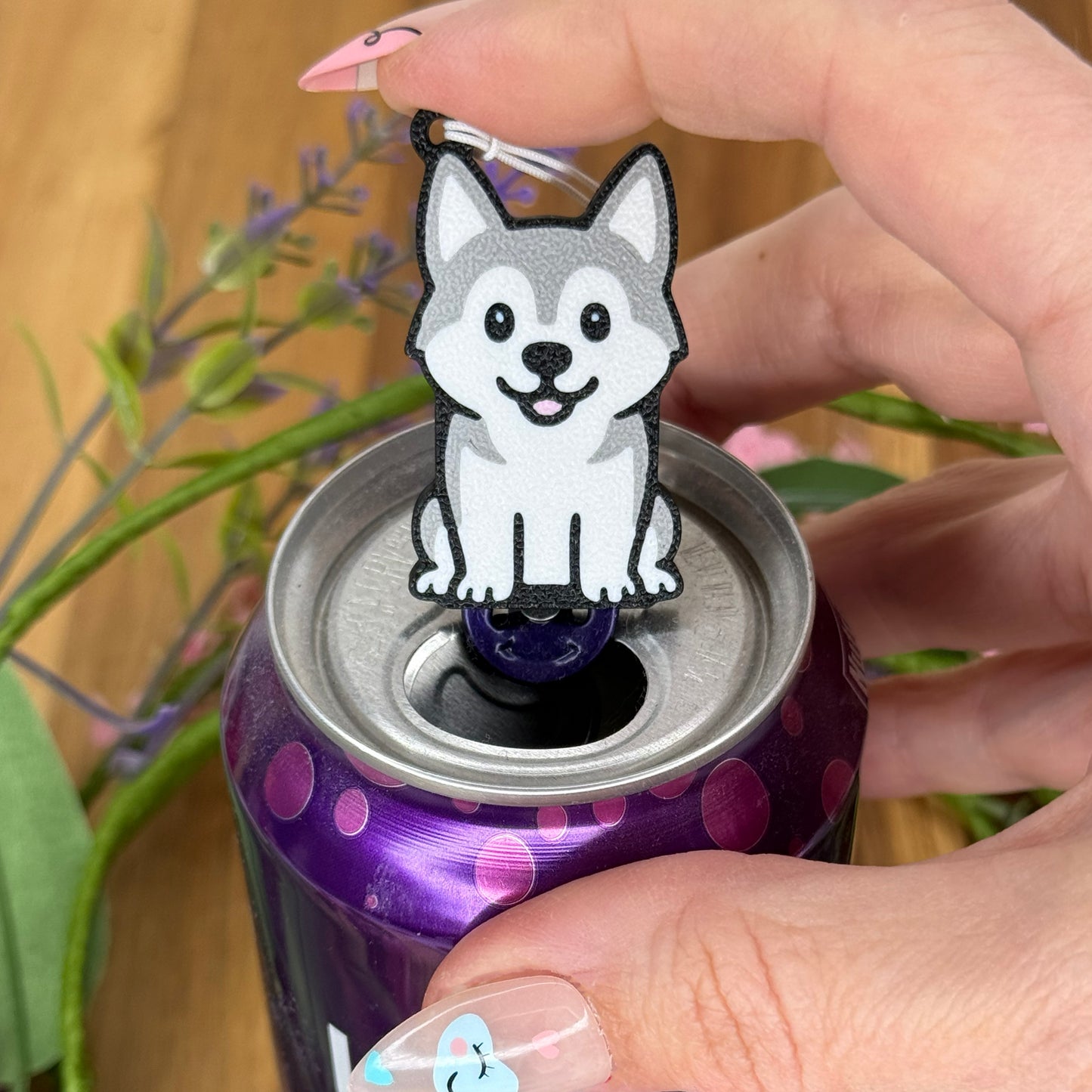 A person with long fingernails rests a finger atop a grey and white Husky design Tab Buddy after using it to open a purple can of sparkling water.
