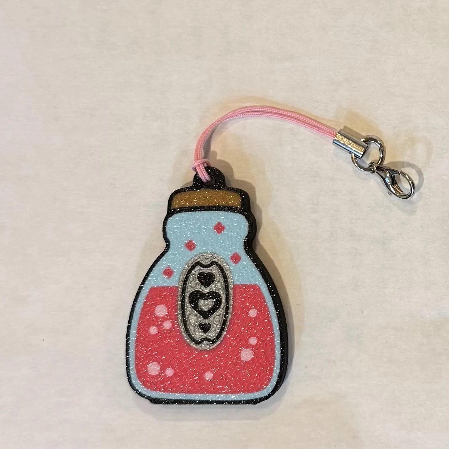 Pink love potion bottle Tab Buddy with keyring strap on a beige background