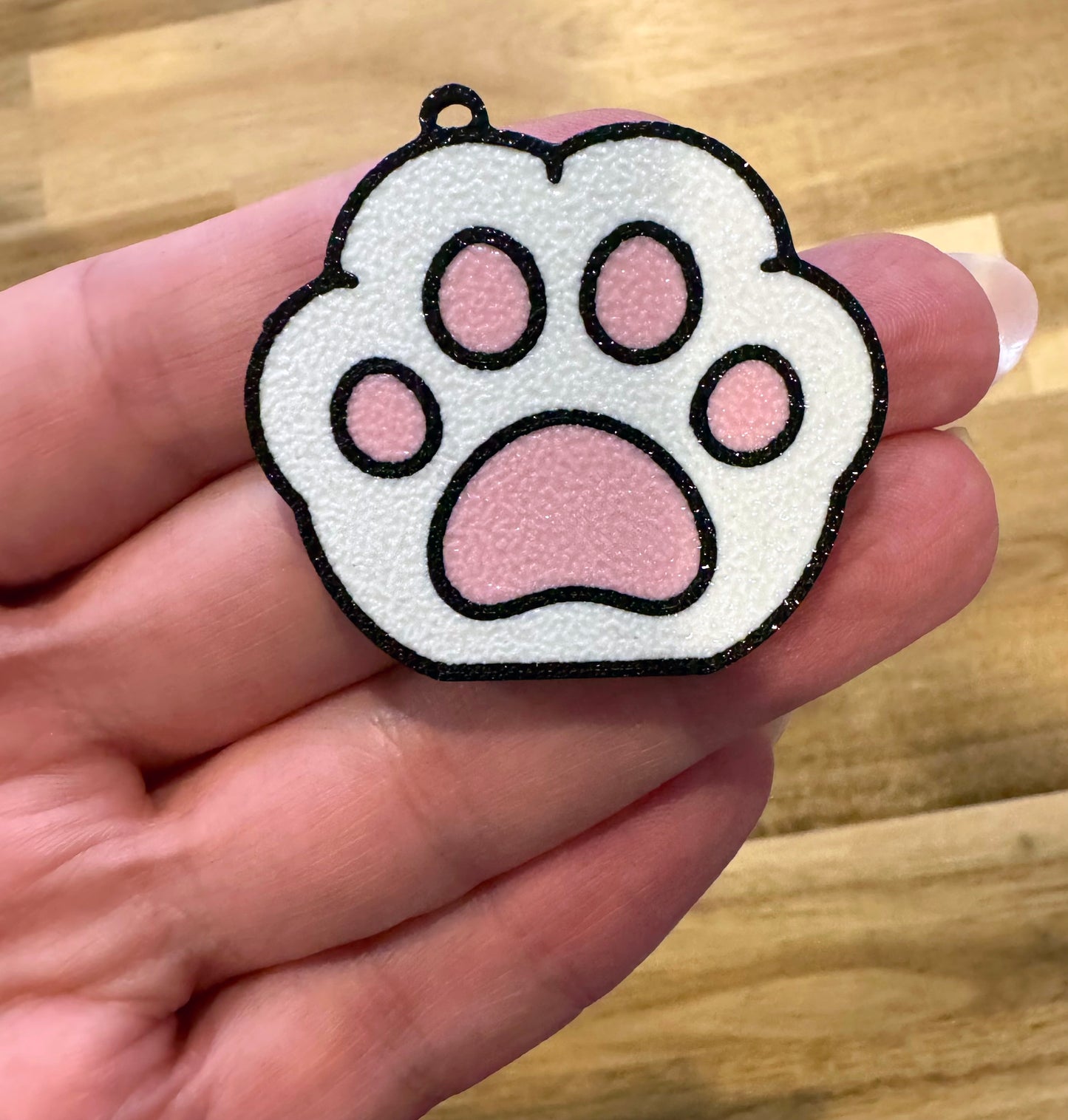 White paw print-shaped Tab Buddy keychain held in a hand on a wooden surface