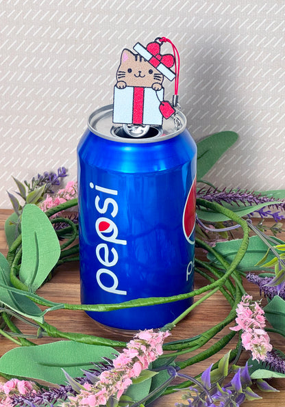 Pepsi can with a cat-shaped Tab Buddy peeking out of a giftbox on top, surrounded by greenery and flowers.