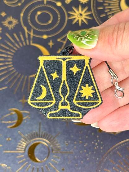 Hand holding a black and gold Libra zodiac Tab Buddy against a background with astrological symbols.