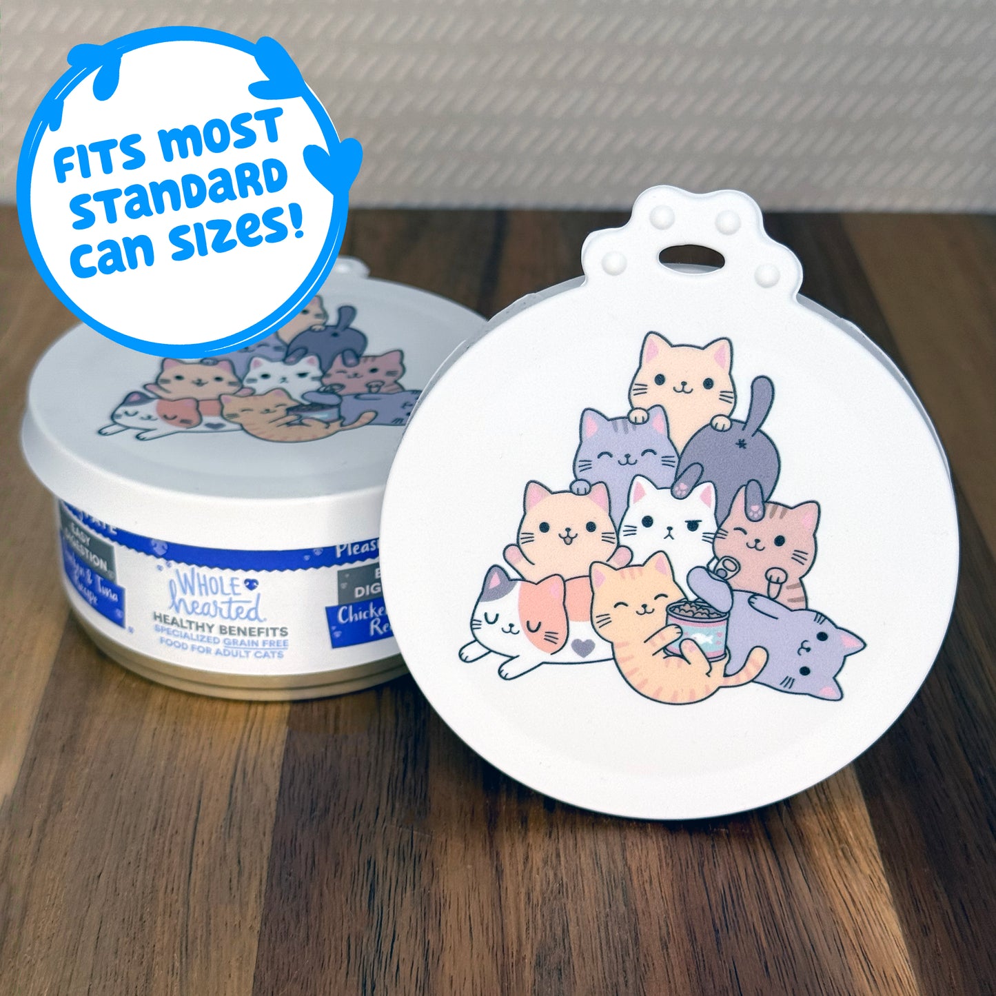 A can lid featuring cute cats piled on top of each other rests in front of a can of cat food with another lid covering the top. Descriptive text reads, "fits most standard can sizes!"