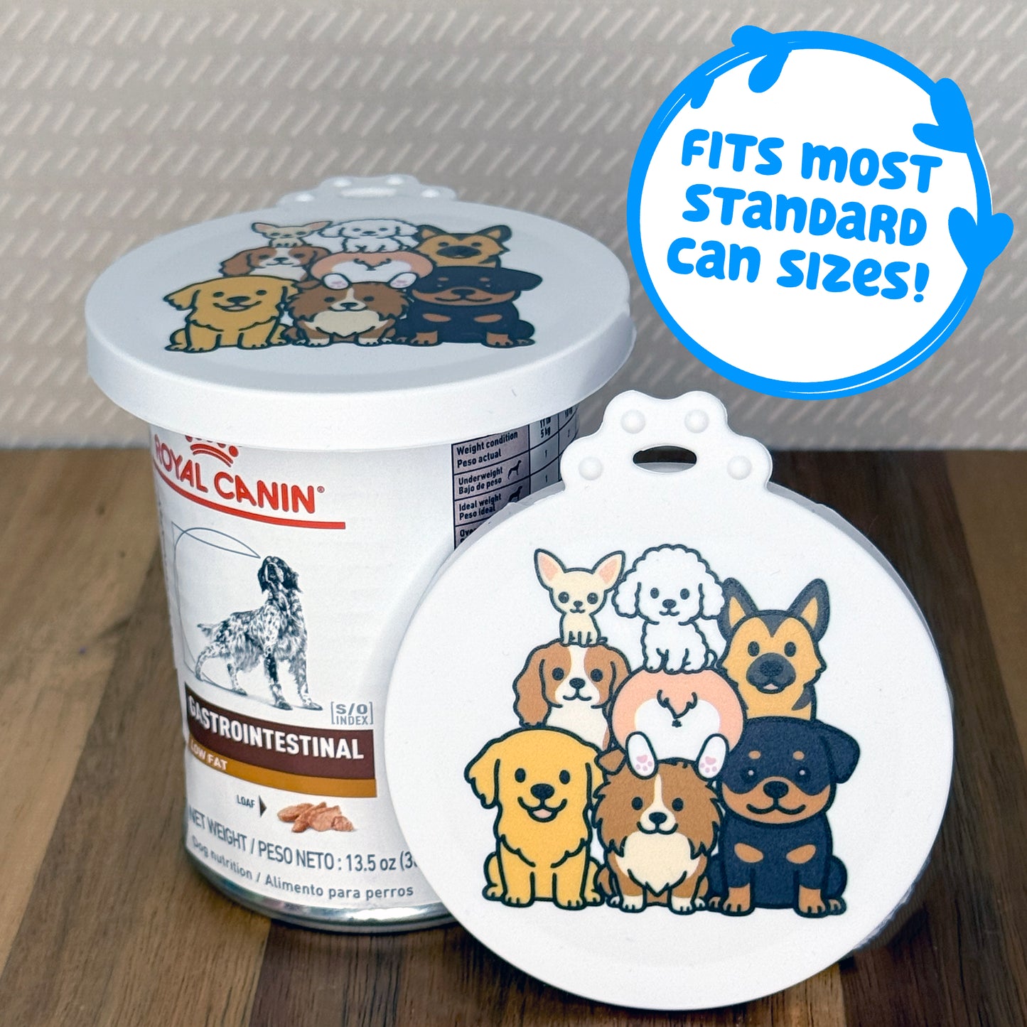 A can lid featuring cute dog breeds piled on top of each other rests in front of a can of dog food with another lid covering the top. Descriptive text reads, "fits most standard can sizes!"