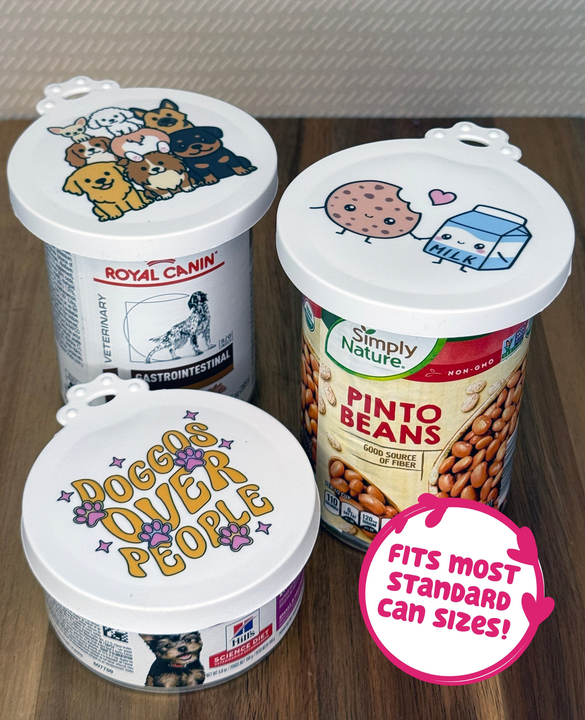 Three food cans of vearious types and sizes are shown with dog- and food-themed resusable can lids sealing their tops. Text bubble reads, "Fits most standard can sizes!"