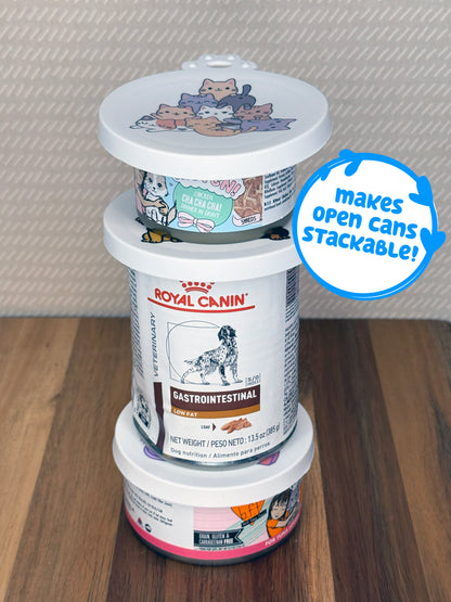 Stack of three pet food cans with a lid featuring cartoon cats, on a wooden surface. Descriptive text reads, "makes open cans stackable!"