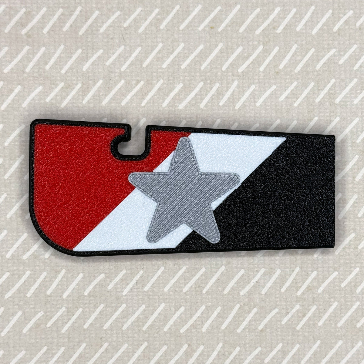A red, white and black flag-themed Tab Buddy XL rests against a beige background.