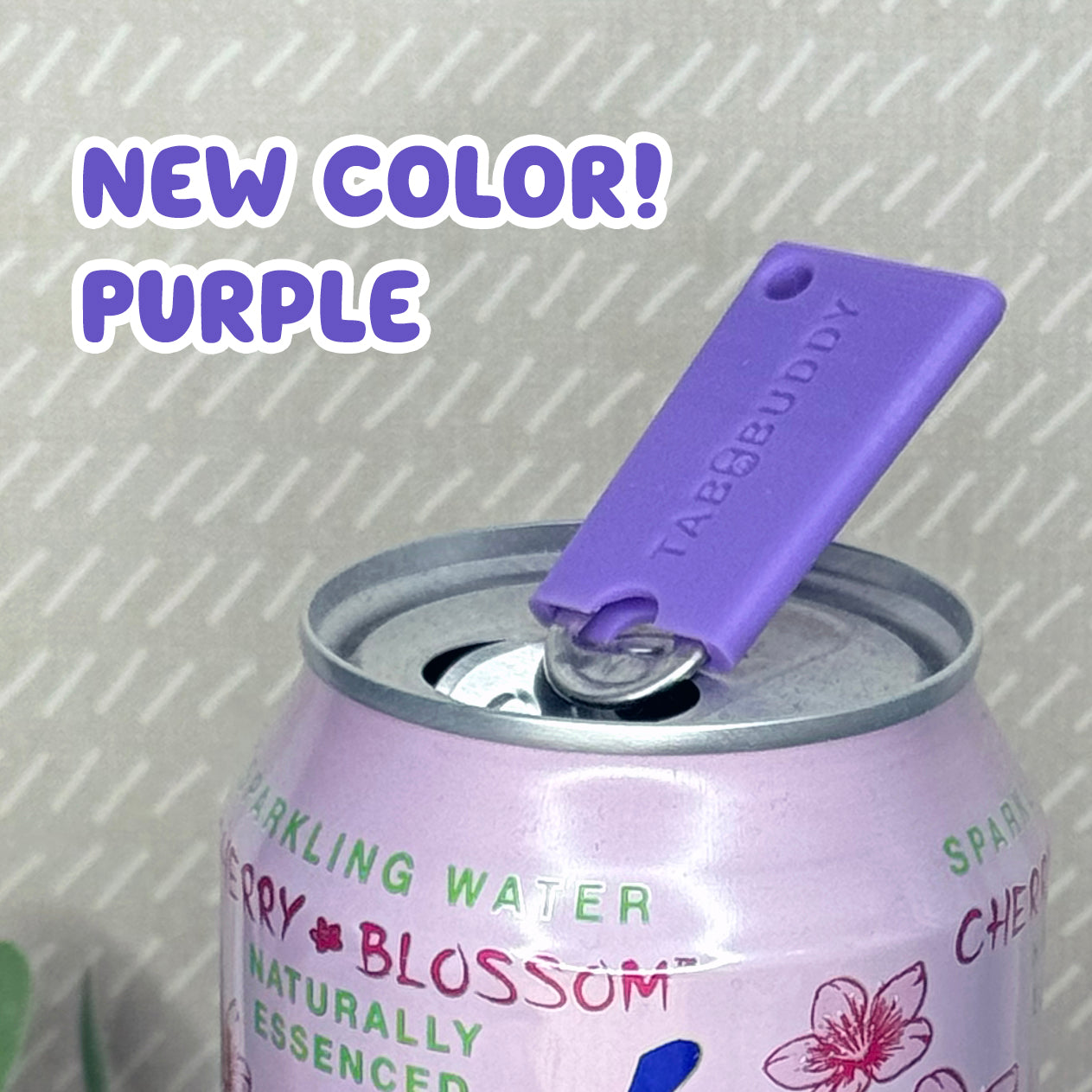 A purple Tab Buddy Mini soda can opener rests atop the tab of an open can of sparkling water with a beige background. Text reads, "New color! Purple"