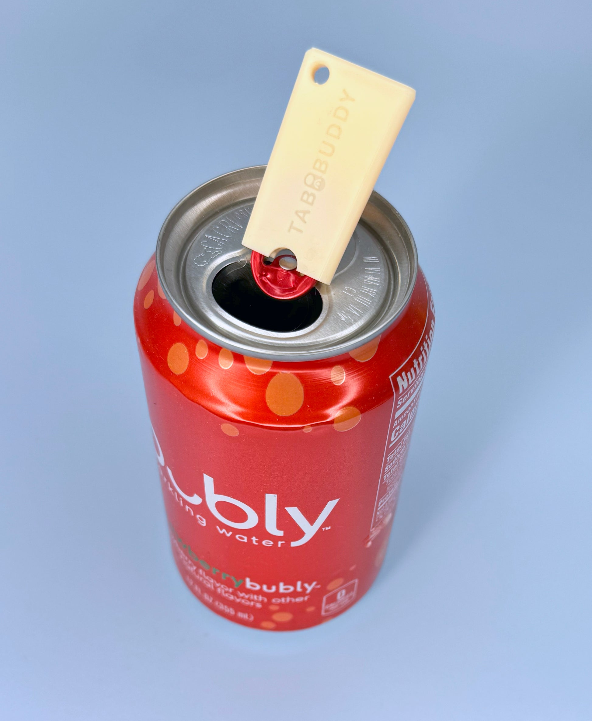 Peach colored Tab Buddy Mini sits atop a red can of Bubly sparkling water with a light blue background