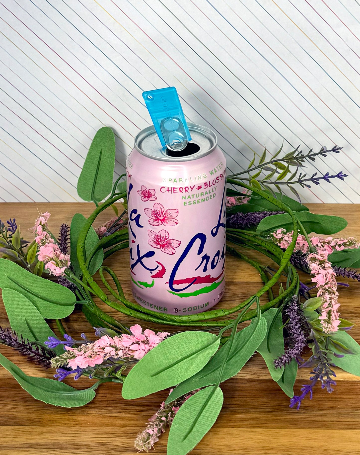 Pink can with Sapphire blue Tab Buddy Mini on a wooden surface with greenery and flowers.
