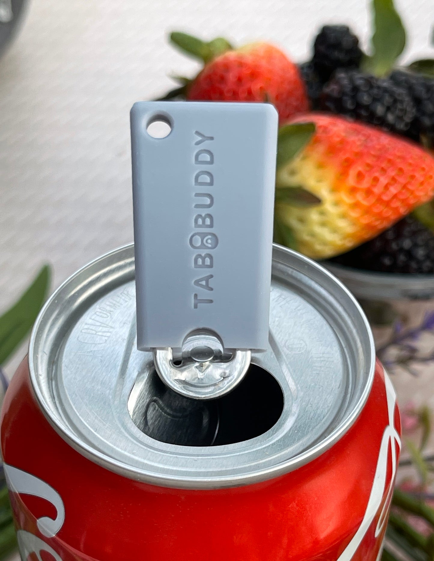 Grey Tab Buddy Mini can opener on a Coca-Cola can with berries in the background