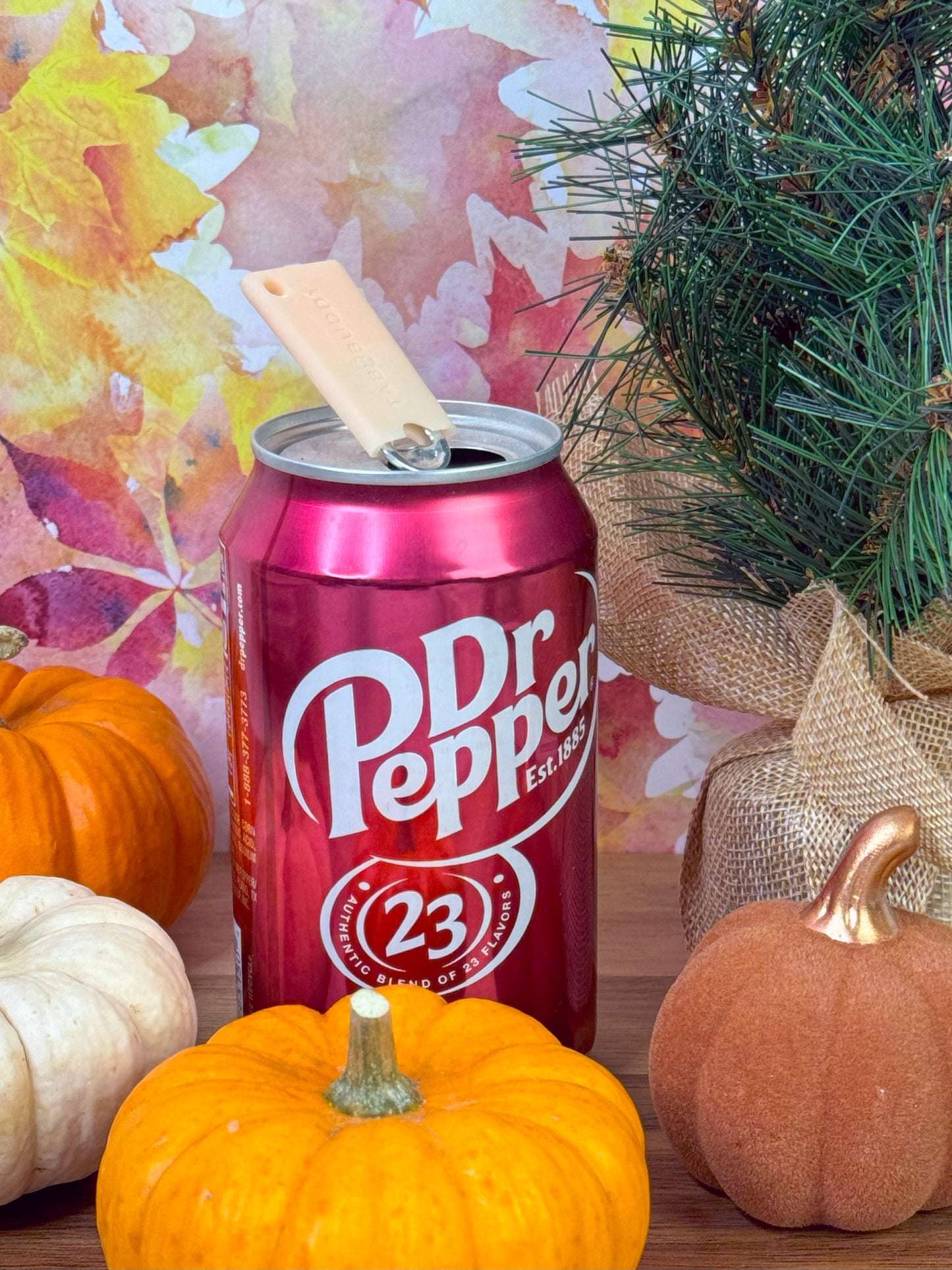 A peach-colored Tab Buddy mini sits atop a Dr Pepper can with pumpkins and a tree in the background