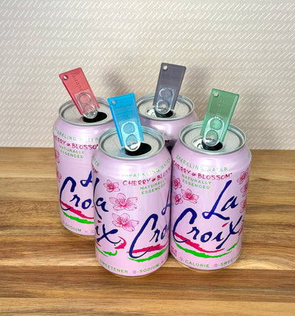 Four pink La Croix cans with colorful transluscent Tab Buddy Minis on a wooden surface.
