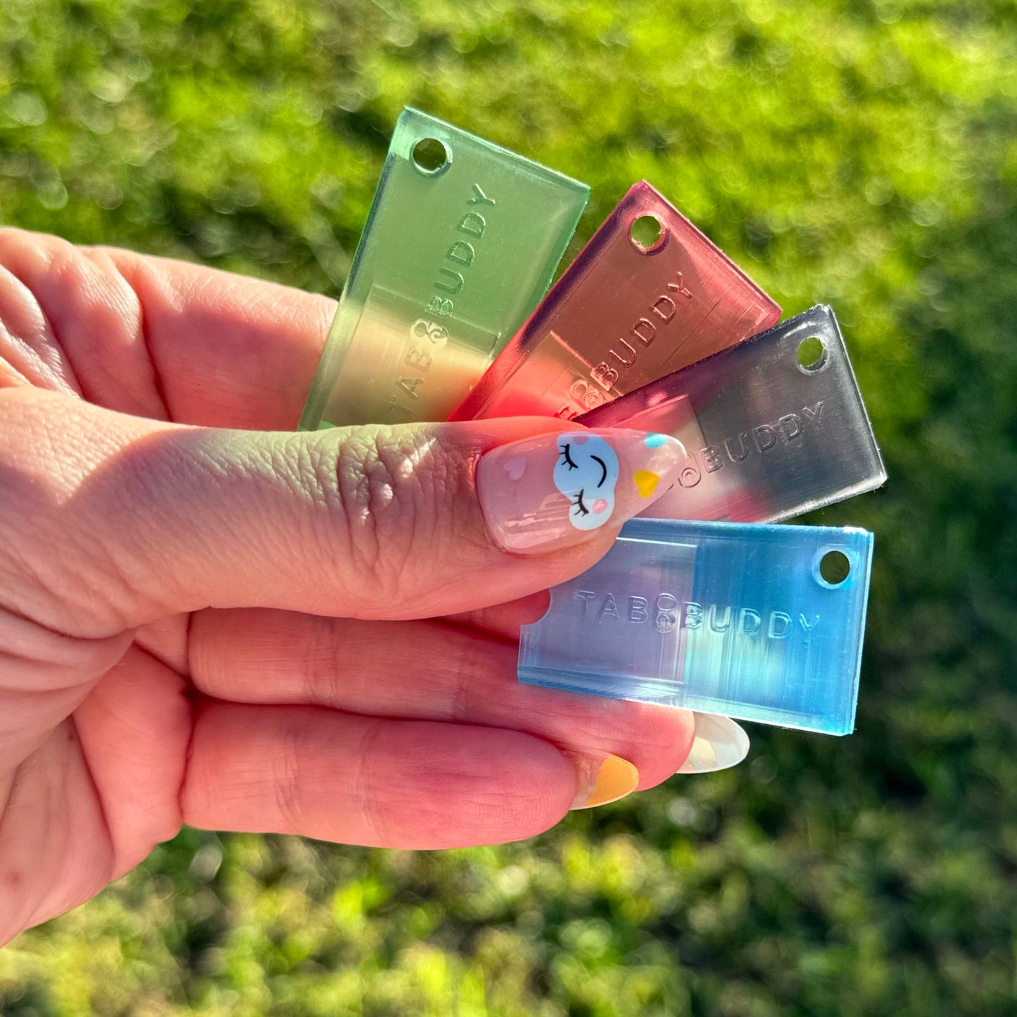 Hand holding four transluscent Tab Buddy Minis with a grassy background