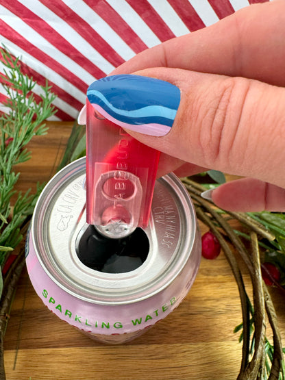 Hand using a Tab Buddy Mini in transluscent Ruby Red on a can of sparkling water with a decorative background