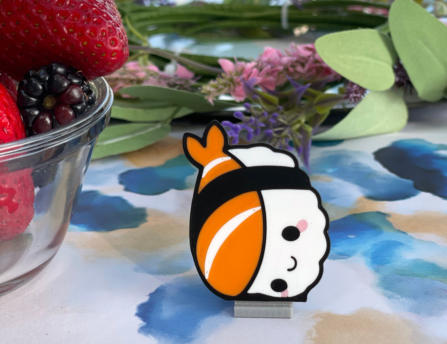 Cartoon nigiri sushi Tab Buddy with a smiling face on a stand with strawberries and flowers in the background