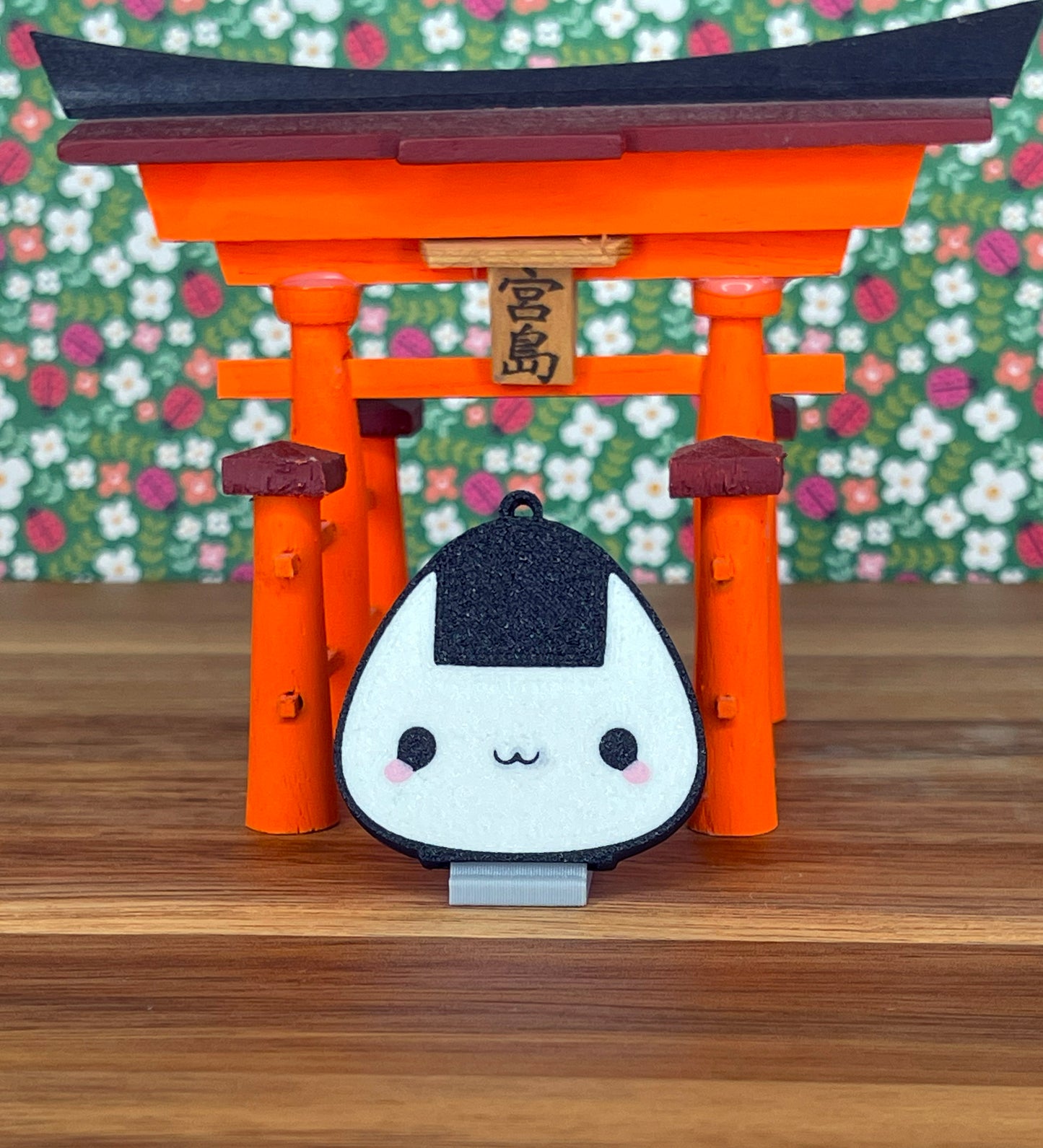 Onigiri-shaped Tab Buddy with a stand in front of an orange torii gate with a floral background