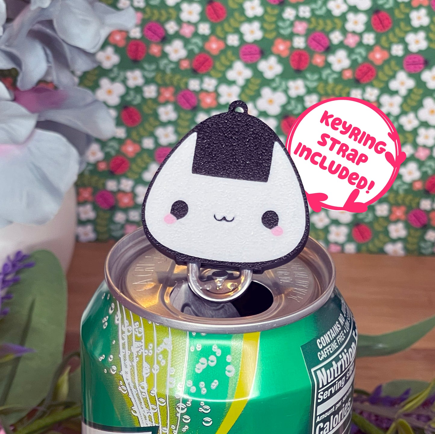 Onigiri-shaped Tab Buddy with keyring strap included sits atop a can with a floral background