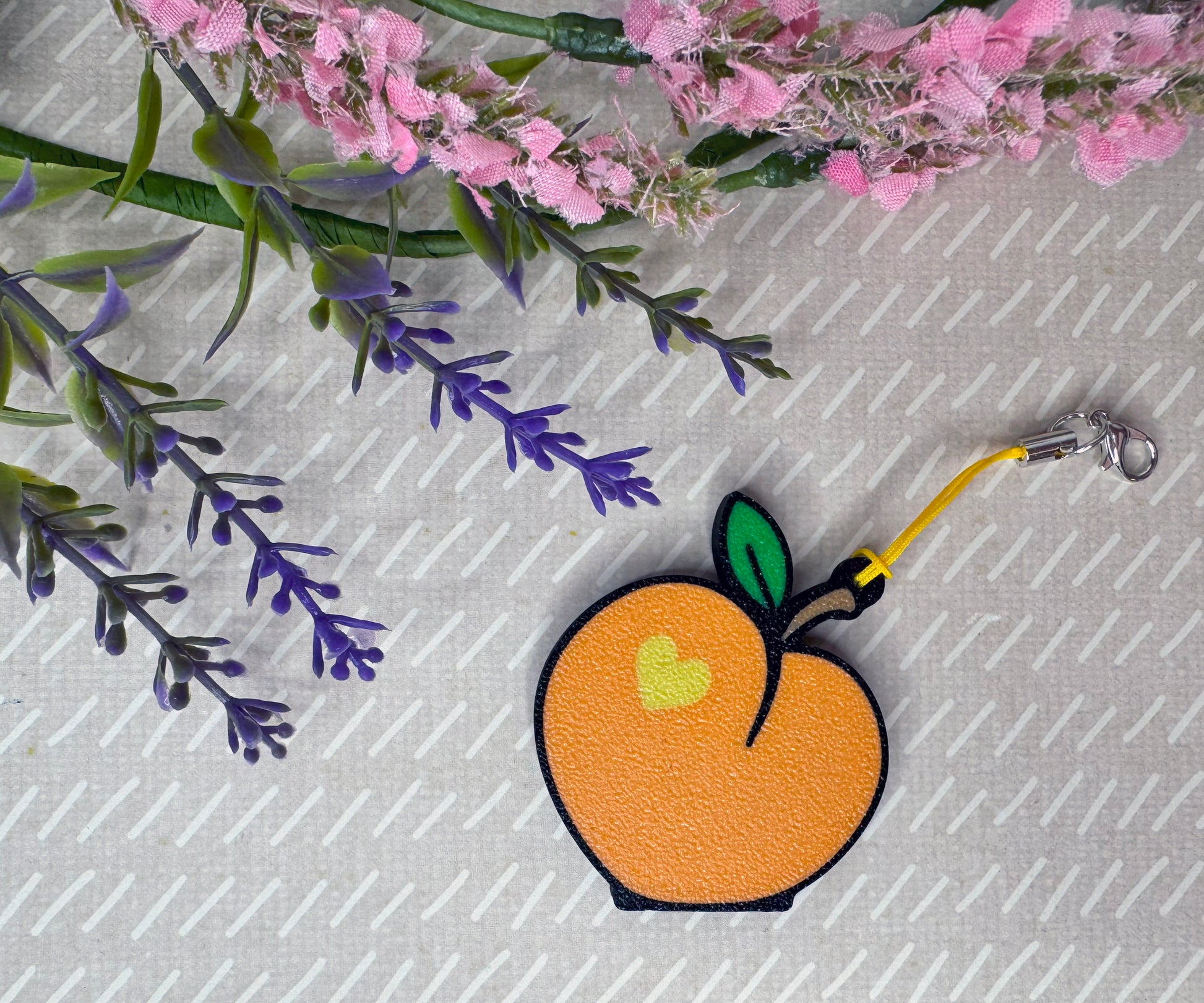 Peach-shaped Tab Buddy keychain on a textured surface with flowers